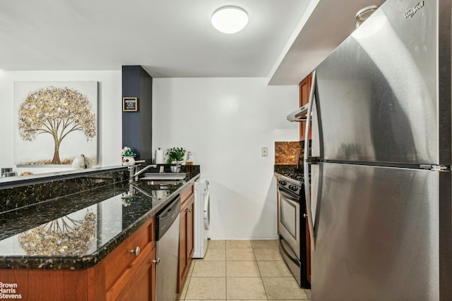 kitchen featuring light tile patterned floors, a sink, appliances with stainless steel finishes, dark stone counters, and washer / clothes dryer