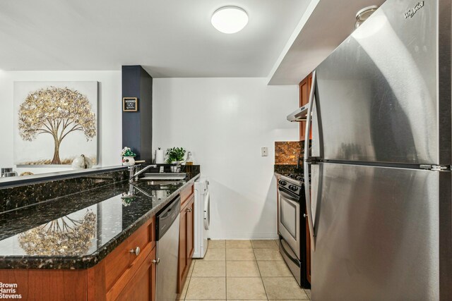 kitchen with stainless steel appliances, washer / clothes dryer, light tile patterned flooring, a sink, and dark stone counters