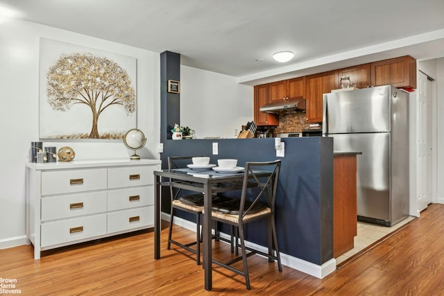 kitchen featuring brown cabinetry, white cabinets, freestanding refrigerator, light wood-type flooring, and under cabinet range hood