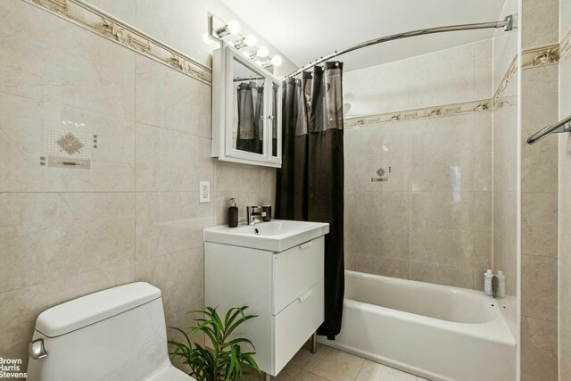 full bathroom featuring toilet, tile patterned floors, shower / bathtub combination with curtain, vanity, and tile walls