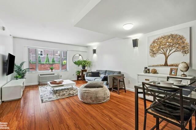 living room with a wall mounted air conditioner, wood finished floors, and baseboards