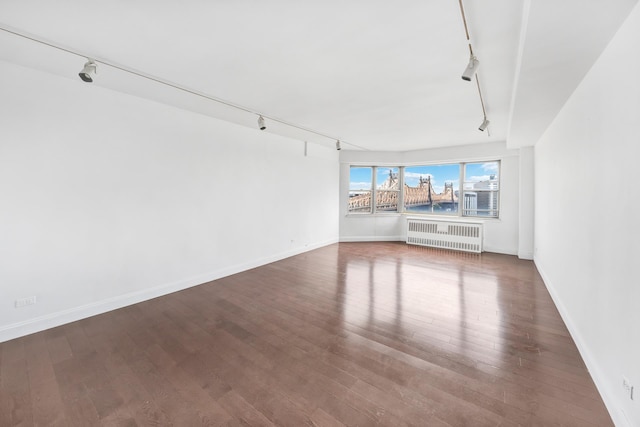 empty room with baseboards, track lighting, wood finished floors, and radiator