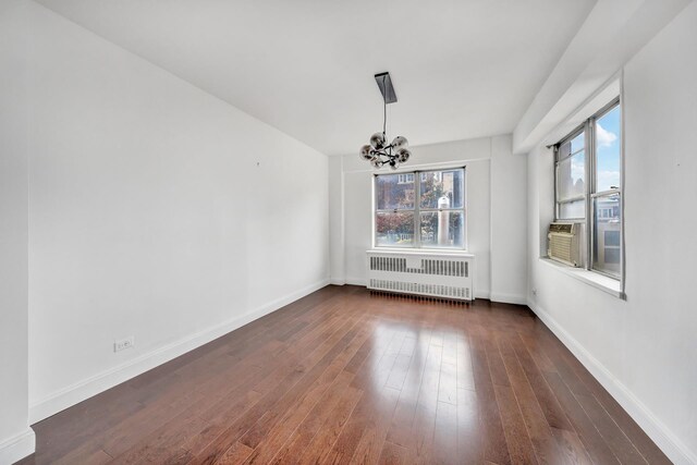 unfurnished dining area featuring baseboards, dark wood finished floors, radiator, cooling unit, and a notable chandelier