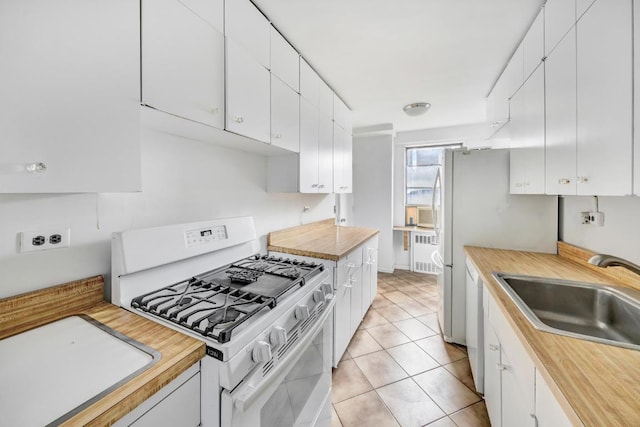 kitchen featuring sink, light tile patterned floors, radiator heating unit, white appliances, and white cabinets