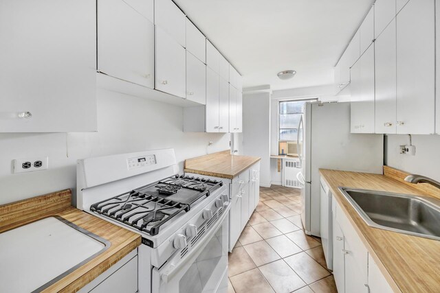 kitchen with light tile patterned floors, radiator heating unit, white cabinets, a sink, and white appliances