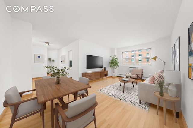 living area with light wood-style floors, a wall unit AC, and baseboards