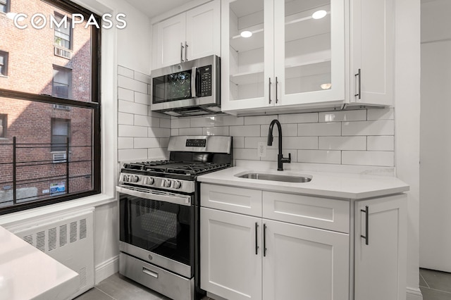 kitchen featuring stainless steel appliances, radiator heating unit, a sink, and white cabinetry