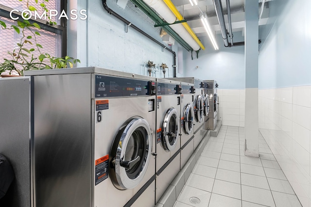 community laundry room featuring tile walls, washer and clothes dryer, and light tile patterned floors