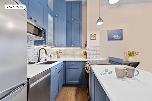 kitchen with appliances with stainless steel finishes, backsplash, blue cabinetry, decorative light fixtures, and sink