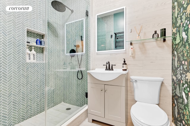 bathroom with toilet, vanity, wood walls, and tiled shower