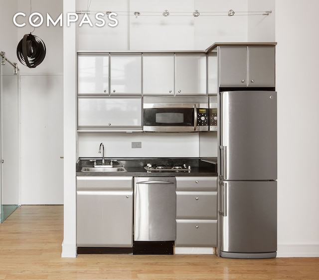 kitchen with light wood-style flooring, gray cabinetry, a sink, appliances with stainless steel finishes, and dark countertops