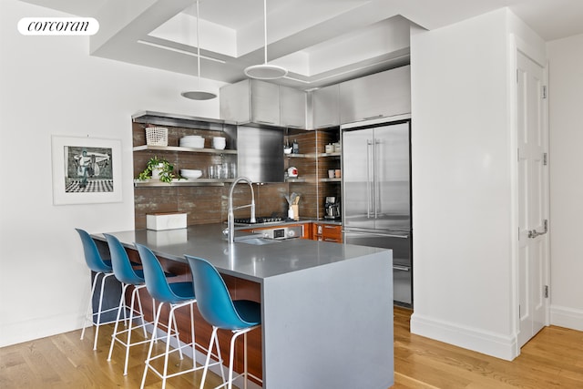 kitchen with a kitchen bar, sink, kitchen peninsula, built in fridge, and light hardwood / wood-style floors