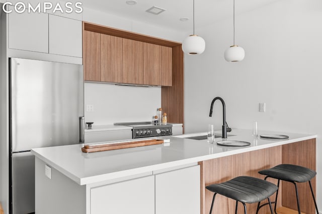 kitchen with decorative light fixtures, white cabinetry, sink, stainless steel fridge, and stove