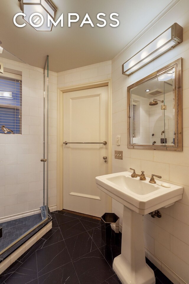 full bathroom with marble finish floor, a shower stall, and tile walls