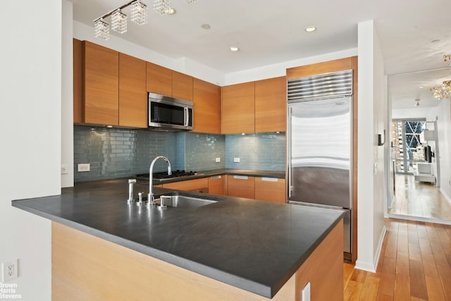 kitchen featuring sink, decorative backsplash, kitchen peninsula, stainless steel appliances, and light hardwood / wood-style flooring