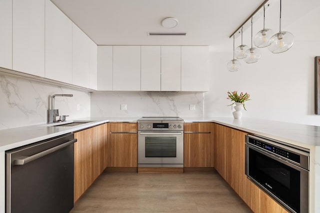 kitchen featuring pendant lighting, stainless steel appliances, light countertops, white cabinets, and a sink