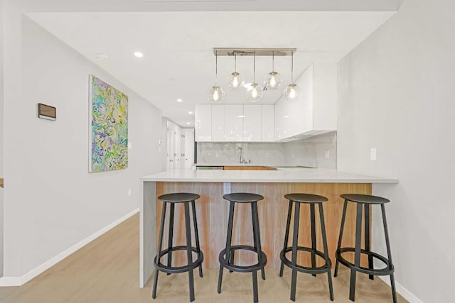 kitchen with a breakfast bar area, tasteful backsplash, hanging light fixtures, kitchen peninsula, and white cabinets