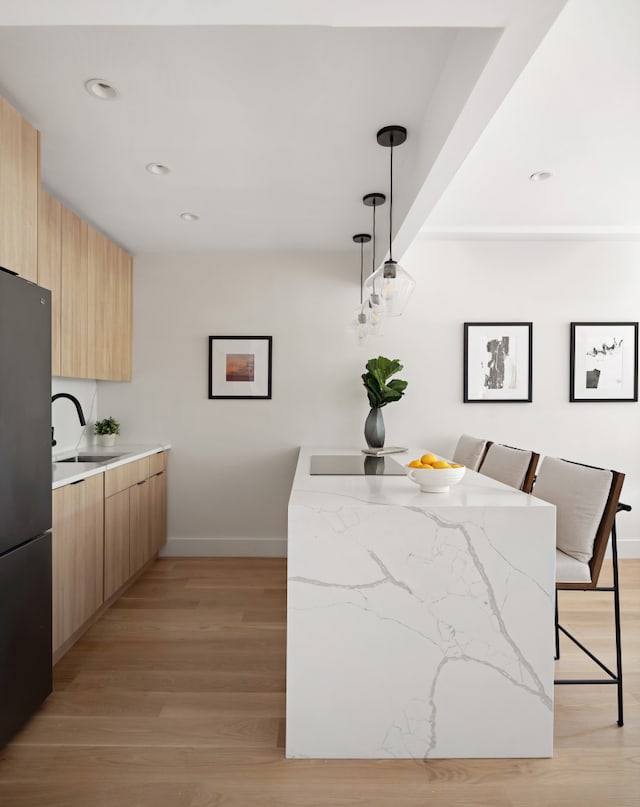 kitchen with a sink, light countertops, freestanding refrigerator, modern cabinets, and decorative light fixtures