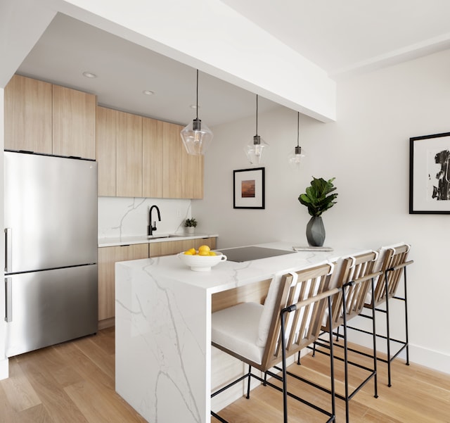 kitchen featuring stainless steel fridge, light brown cabinets, a kitchen bar, and light wood-style floors