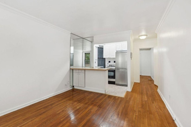 kitchen with hardwood / wood-style floors, appliances with stainless steel finishes, kitchen peninsula, white cabinets, and ornamental molding