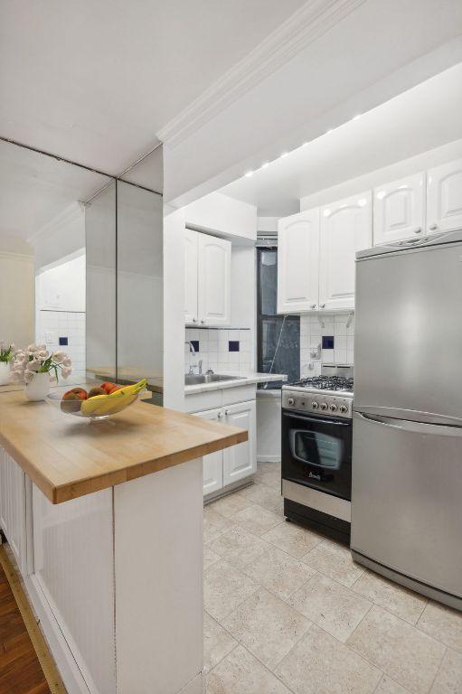 kitchen with stainless steel appliances, ornamental molding, backsplash, white cabinets, and wooden counters