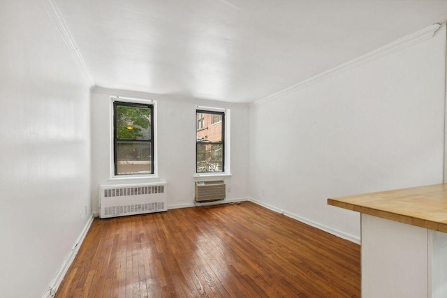 spare room with a wall unit AC, crown molding, radiator heating unit, and wood-type flooring