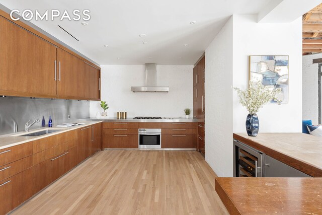 16 Jay St Unit 1, New York City, NY 10013 - kitchen with wall chimney exhaust hood, stainless steel oven, brown cabinets, light wood-style flooring, and beverage cooler