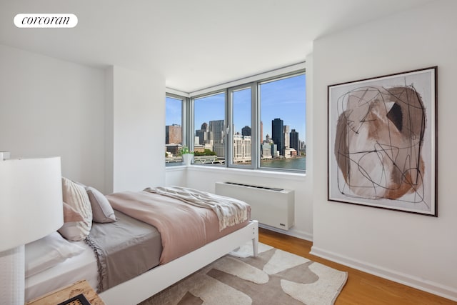 bedroom with light wood finished floors, baseboards, visible vents, radiator, and a city view