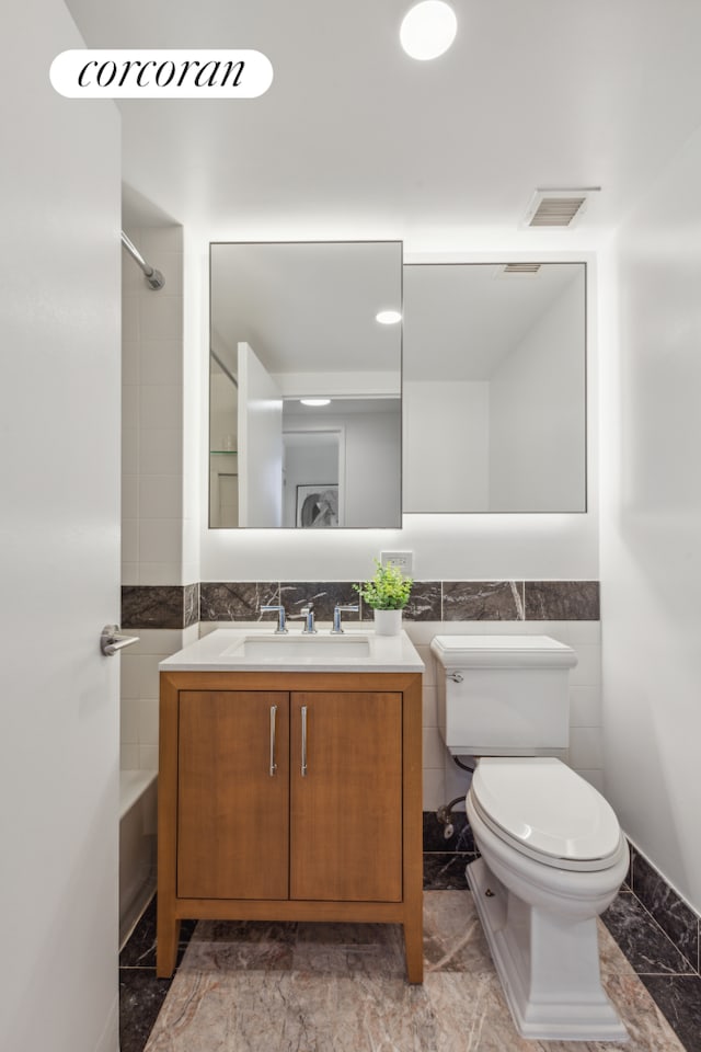 425 Main St Unit 12D, New York City, NY 10044 - full bathroom featuring tile walls, marble look tile flooring, vanity, bathtub / shower combination, and a wainscoted wall