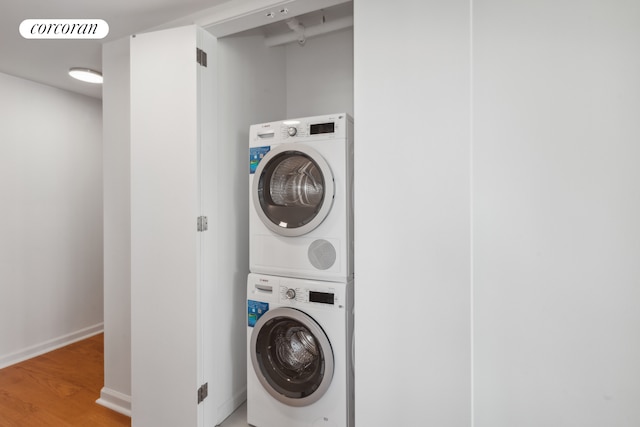 clothes washing area featuring stacked washer and dryer, visible vents, light wood-style floors, laundry area, and baseboards