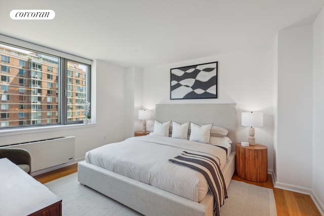 bedroom with radiator heating unit, wood finished floors, visible vents, and baseboards