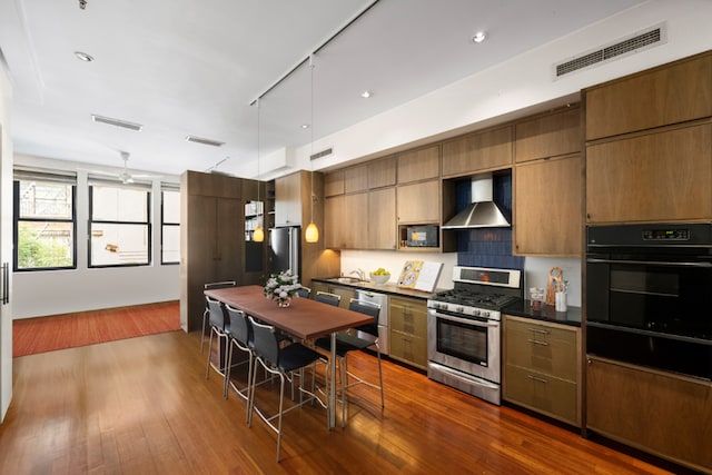 kitchen with decorative light fixtures, sink, stainless steel appliances, dark wood-type flooring, and wall chimney exhaust hood