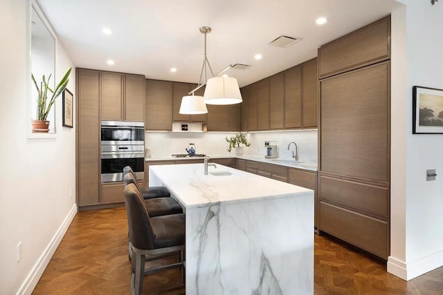 kitchen featuring hanging light fixtures, an island with sink, dark parquet floors, and stainless steel appliances