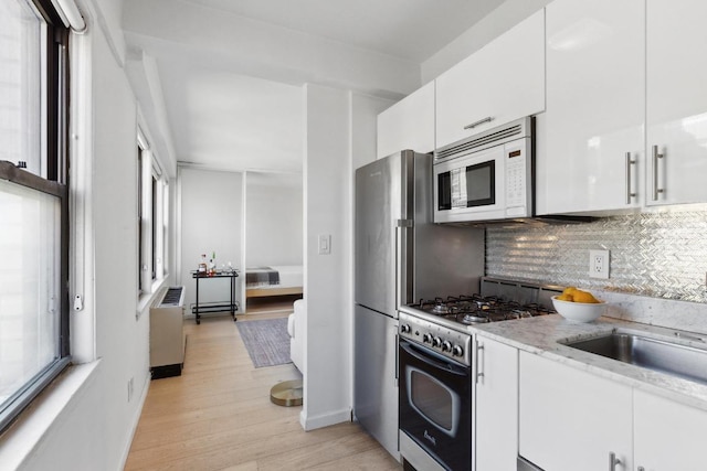 kitchen featuring tasteful backsplash, light stone counters, light hardwood / wood-style flooring, appliances with stainless steel finishes, and white cabinets