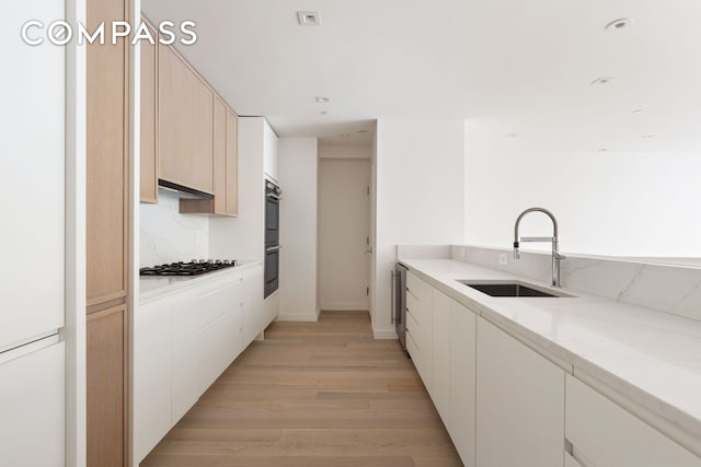 kitchen with light stone countertops, light wood-style flooring, stainless steel appliances, a sink, and backsplash