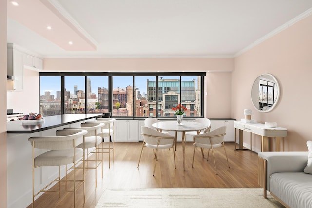 dining room featuring light wood-type flooring, a healthy amount of sunlight, a city view, and crown molding