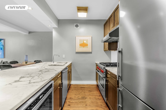 kitchen with beverage cooler, light wood-style floors, stainless steel appliances, under cabinet range hood, and a sink