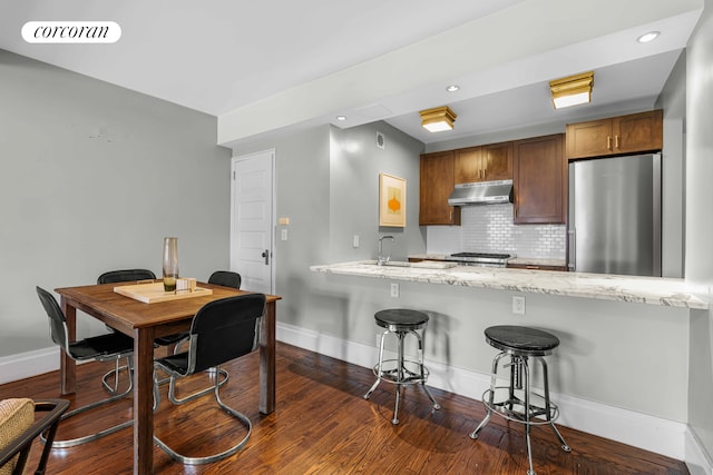 kitchen with visible vents, backsplash, freestanding refrigerator, a peninsula, and under cabinet range hood