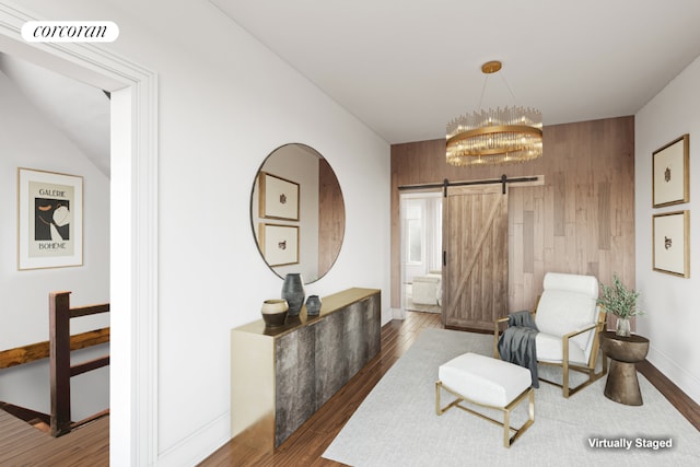 living area featuring a barn door, dark wood-type flooring, an inviting chandelier, and wood walls