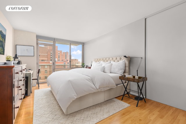 bedroom with a wall of windows, light wood-type flooring, visible vents, and a city view