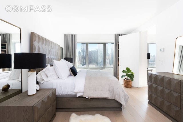 bedroom featuring light wood finished floors, a city view, and connected bathroom