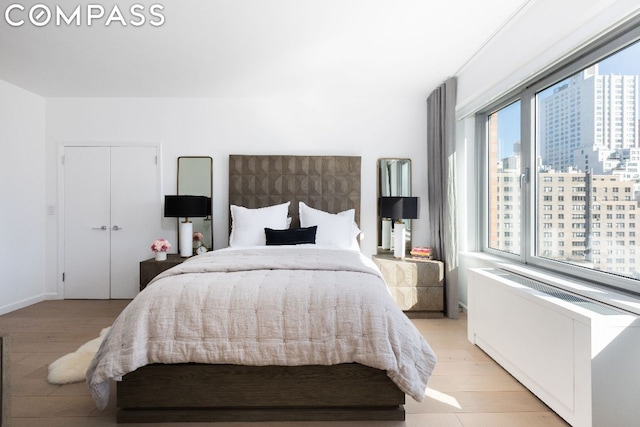 bedroom with a closet, light wood-type flooring, a view of city, and radiator heating unit