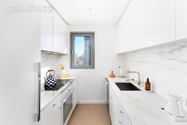kitchen with white cabinets, light wood finished floors, a sink, black electric stovetop, and white oven