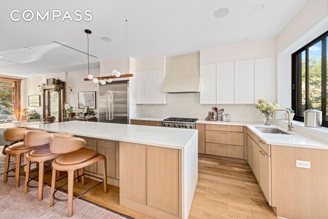 kitchen featuring white cabinets, a center island, stainless steel built in refrigerator, premium range hood, and sink