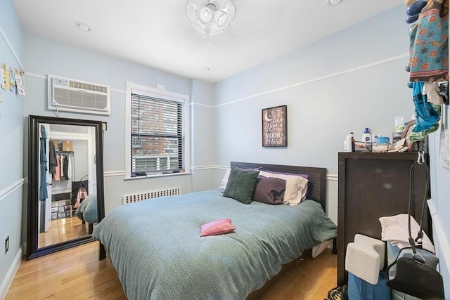 bedroom featuring a wall mounted air conditioner, radiator, and light hardwood / wood-style flooring