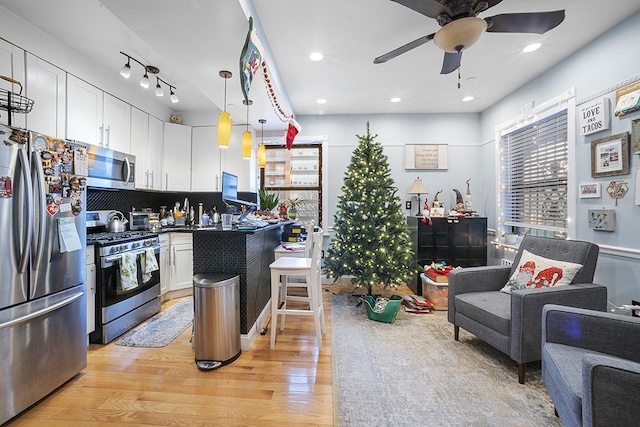 kitchen featuring stainless steel appliances, tasteful backsplash, hanging light fixtures, light wood-style floors, and white cabinets