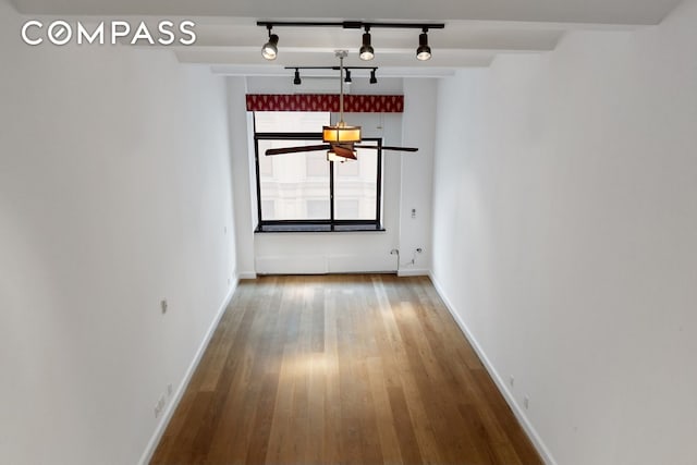 unfurnished dining area with track lighting, wood finished floors, and baseboards