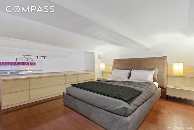 bedroom featuring rail lighting and dark wood finished floors