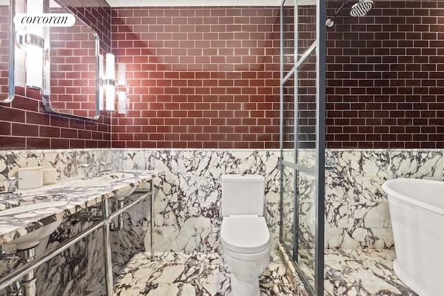 bathroom with toilet, marble finish floor, a tile shower, a freestanding tub, and tile walls