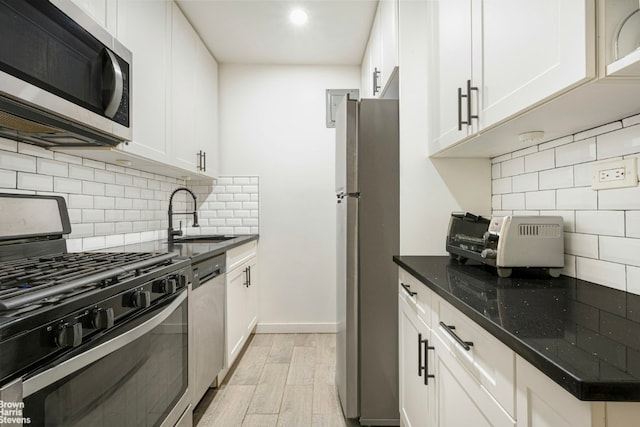 kitchen with sink, white cabinets, dark stone counters, stainless steel appliances, and light hardwood / wood-style flooring